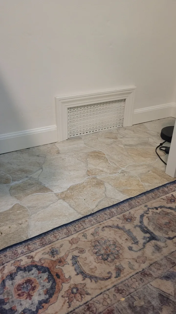 White baseboard and a painted trim surround at a low wall vent, meeting the stone tile floor.