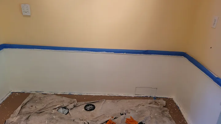 Smoothed lower wall finish with blue masking tape along the upper edge and protection over the floor.