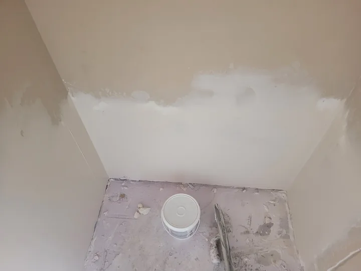 Patched kitchen wall corner with fresh joint compound above the unfinished floor area.