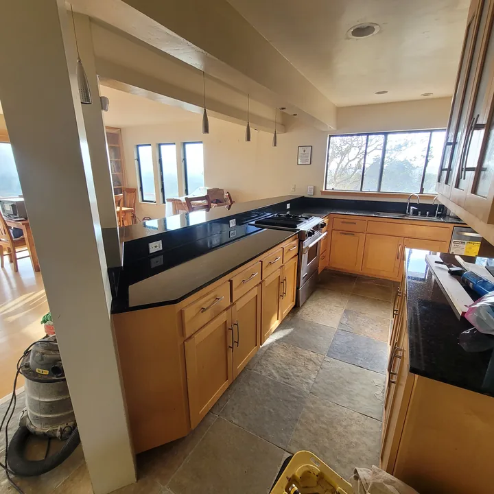 Restored kitchen with varied slate flooring, warm wood cabinetry, dark countertops, and appliances in place.
