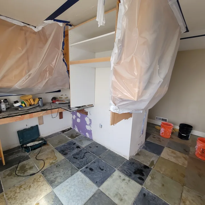 Replacement floor tiles being fitted in the kitchen among tools, buckets, and protected work areas.