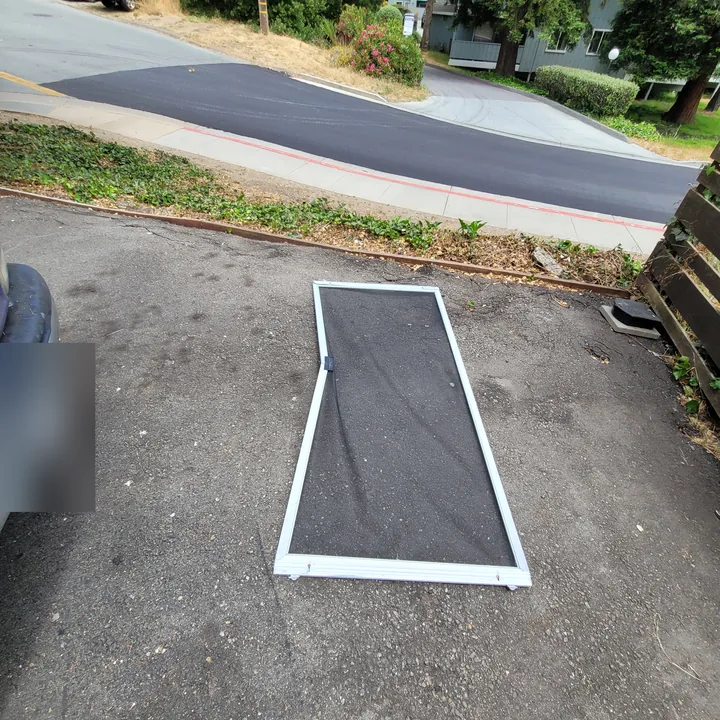 Damaged screen door lying on a driveway before repair.