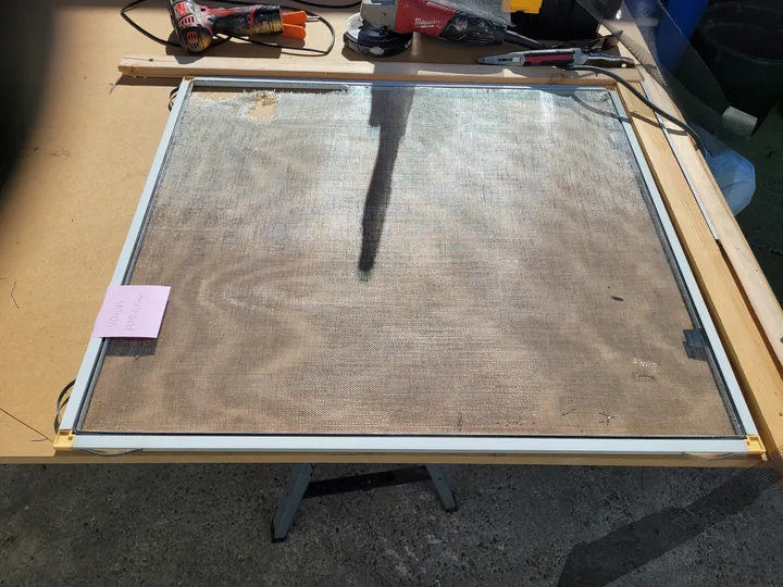Screen held flat in a custom jig on the workbench, with tools nearby.