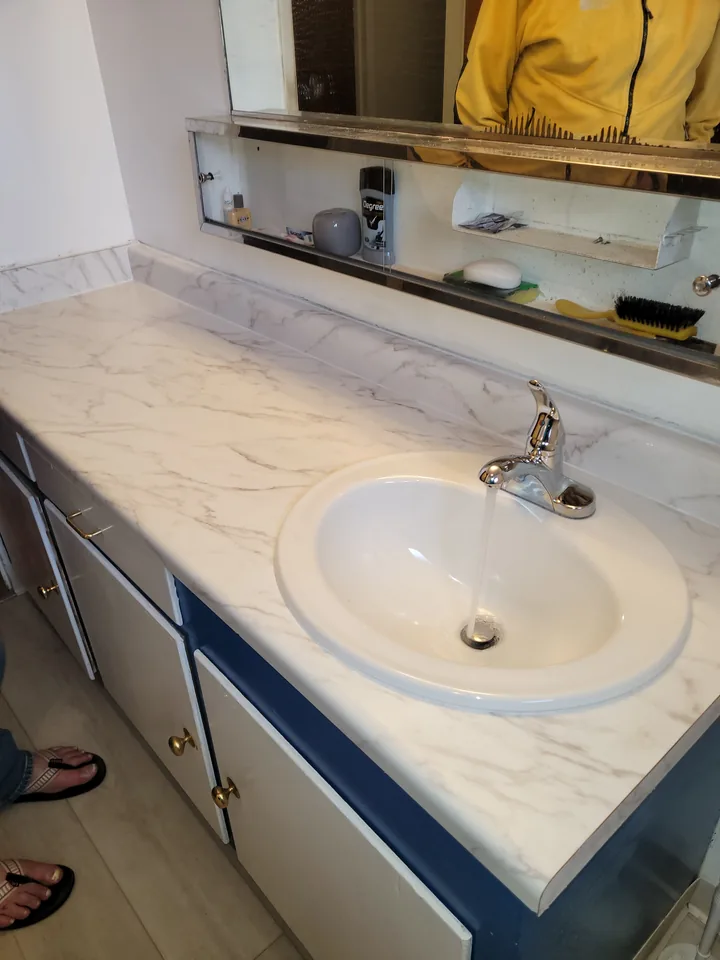 Finished bathroom vanity with a new light-patterned countertop, white basin, and chrome faucet.